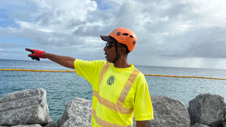 Breakwater worker pointing across the Bridgetown fisheries marina from beside newly placed armour rock