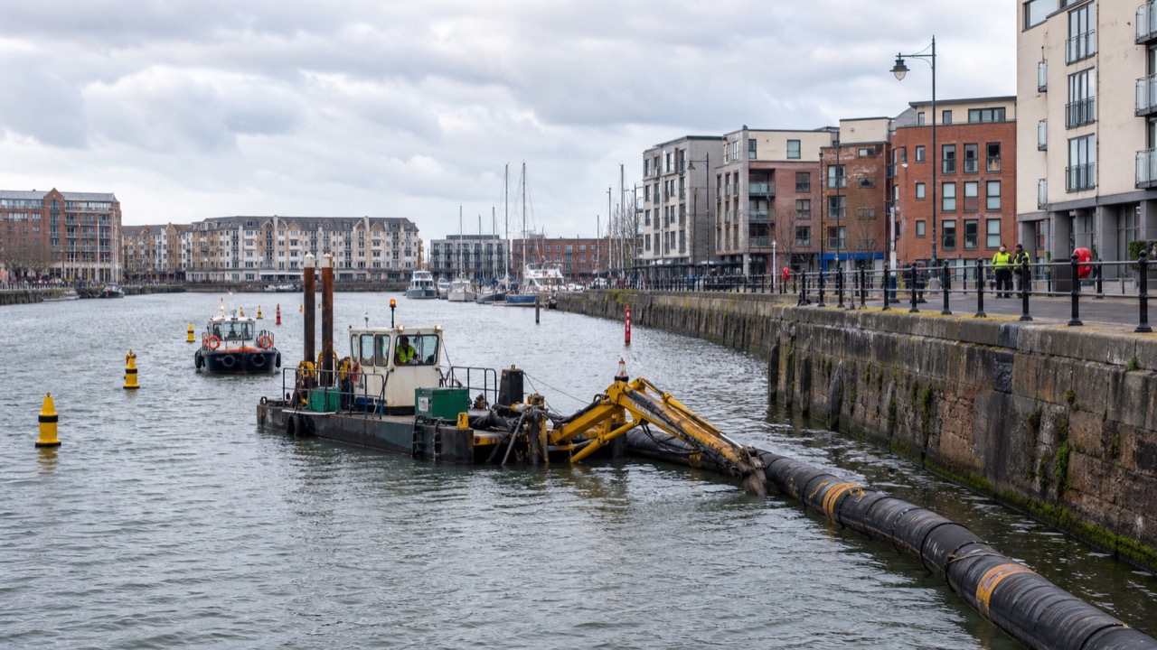 A Bullo-linked dredger working along Bristol Floating Harbour with a floating pipeline, marked navigation restriction and support workboat