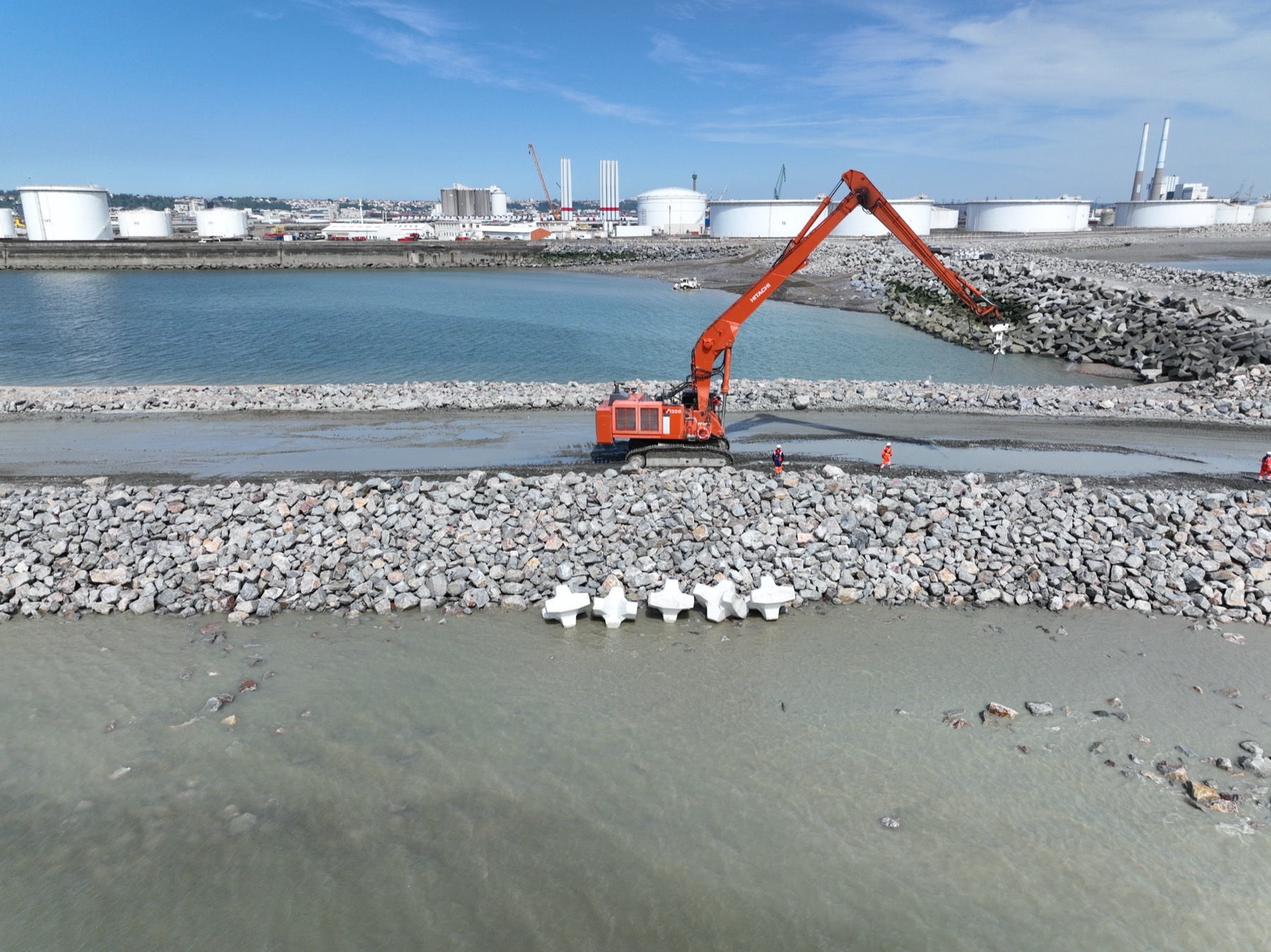Long-reach excavator placing the first concrete Accropode units on the active Port 2000 Chatiere dike workfront at Le Havre