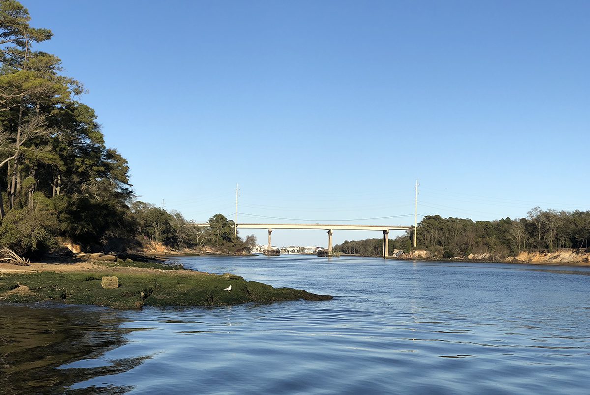 Snow's Cut looking east toward the US 421 bridge, with eroded wooded banks on both sides of the navigation channel