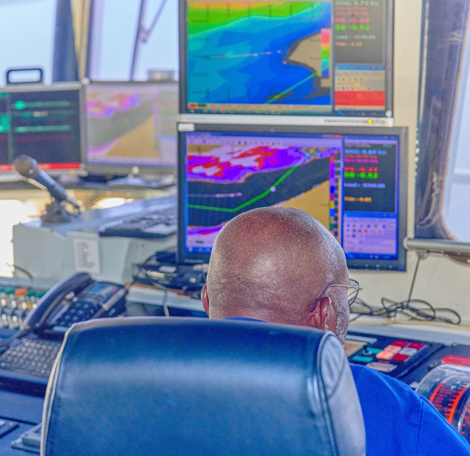 CVM dredging operator seated at a control console with bathymetric, navigation-channel, and vessel-system displays