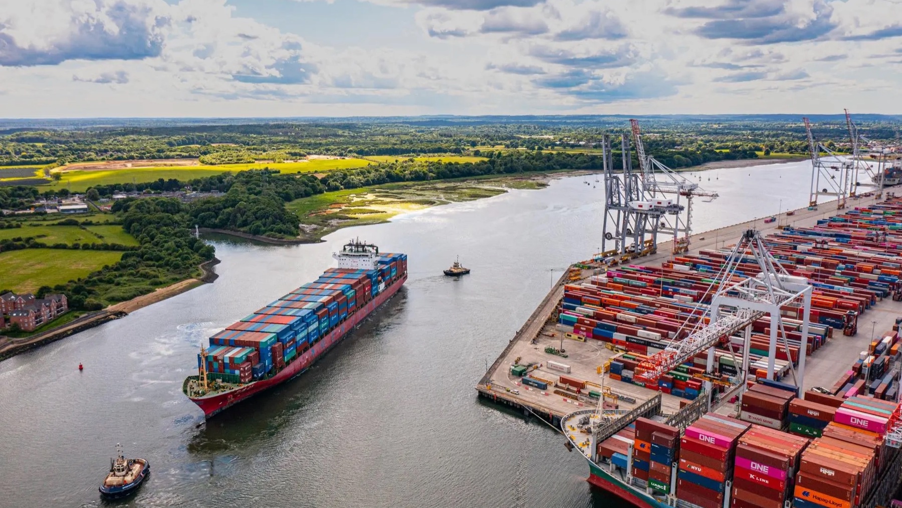 Container vessel, tugs, quay cranes, and terminal stacks at a DP World port operation