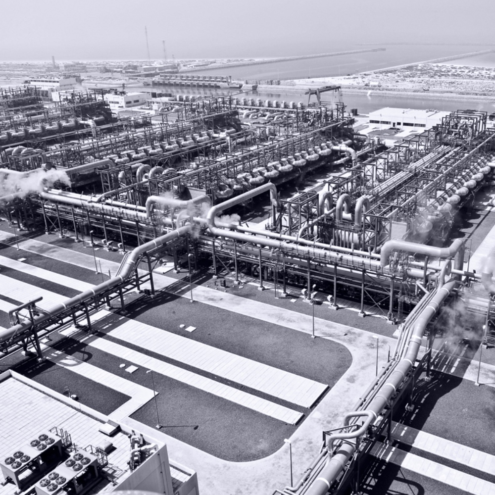 Aerial view across process units, pipework and seawater-side channels at the Al Taweelah Power and Desalination Complex in Abu Dhabi