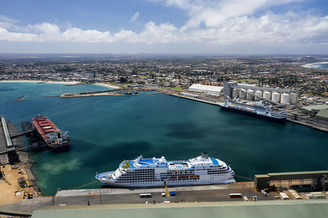 Aerial view across Geraldton Port showing operating commercial berths, cargo facilities and passenger vessels inside the harbour