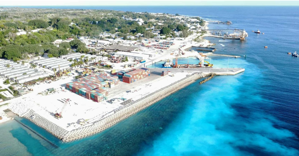 Northwest aerial view of Aiwo Port showing the new wharf and basin, container yards, breakwater protection and the older phosphate-loading structures