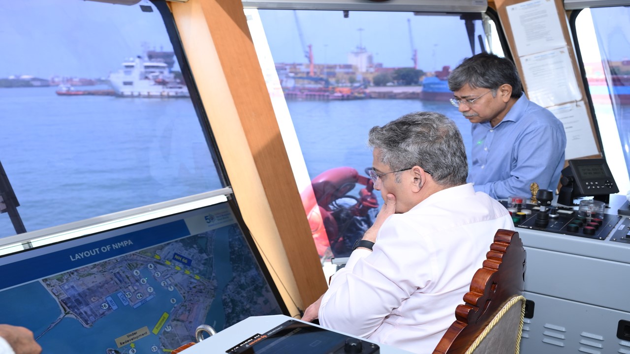 New Mangalore Port officials and a visiting ministry secretary review the port layout with the working harbour visible through the windows