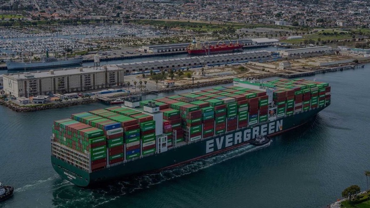 Container ship transiting Los Angeles Harbor with cargo terminals, rail infrastructure and breakwater-protected water in view