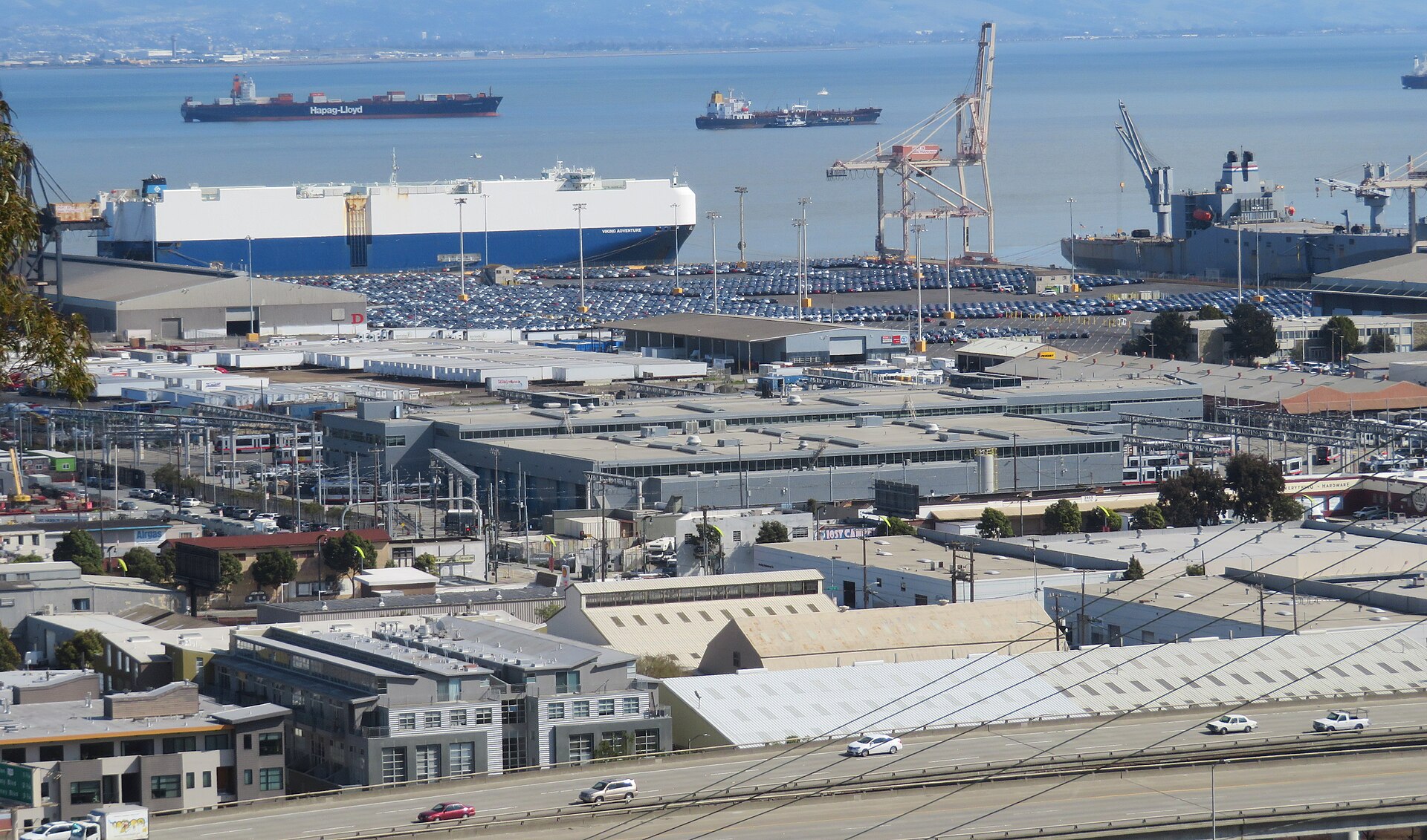 Port of San Francisco Pier 80 vehicle terminal and cargo ships on San Francisco Bay viewed from Potrero Hill, with Muni Metro East in the foreground