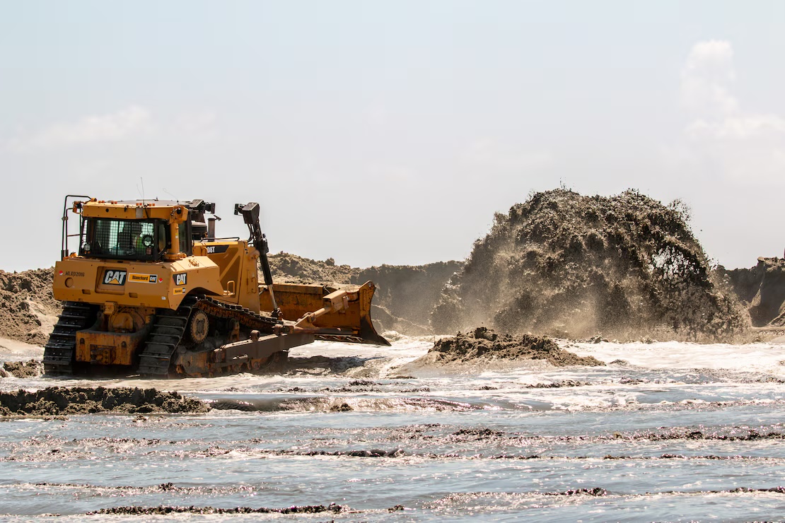 A bulldozer shapes newly placed sand while a beachfill pipeline discharges material during the 2024 Folly Beach renourishment works